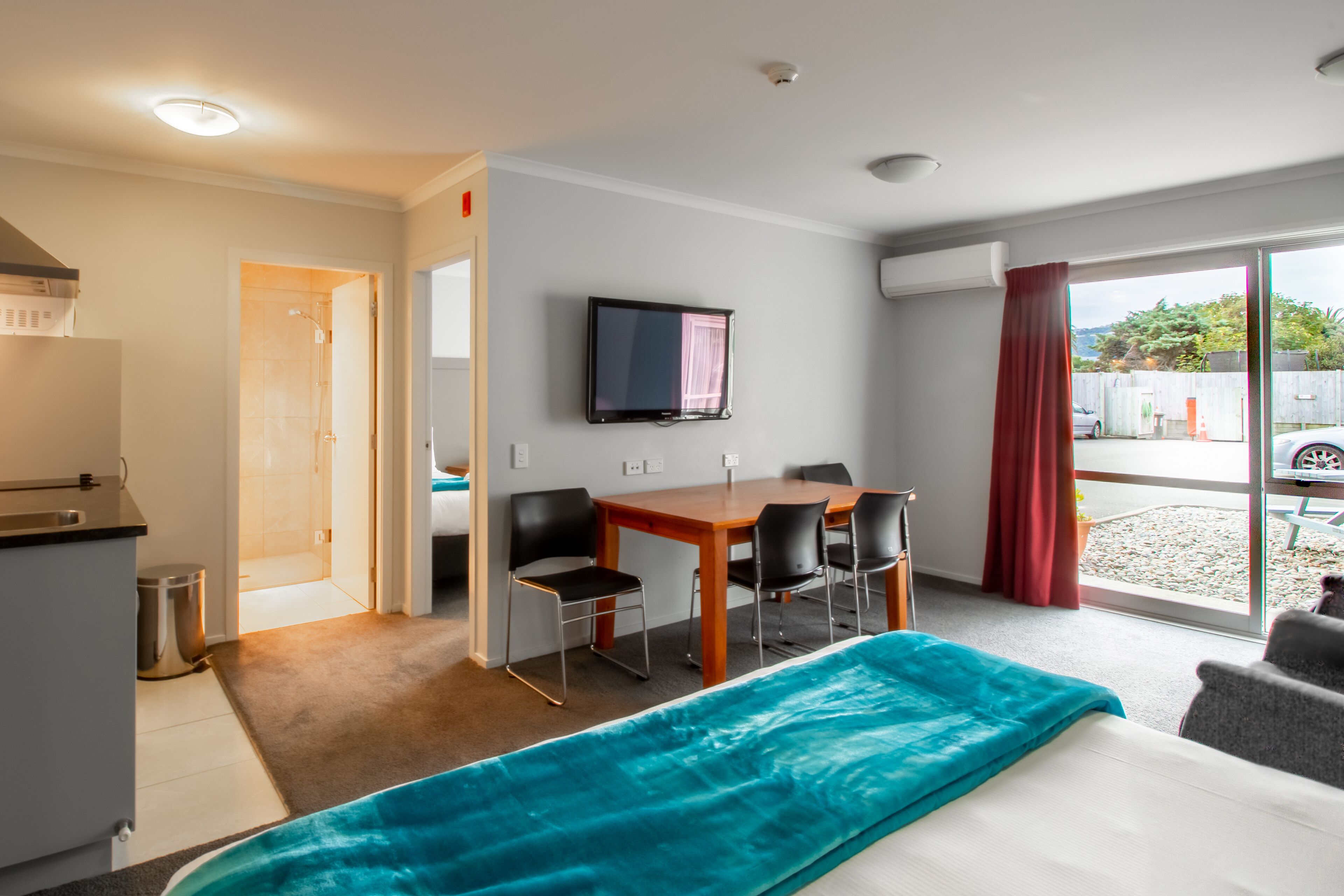 A hotel room with a bed, a desk with chairs, a television, and a view of the outside.