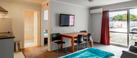 A hotel room with a bed, a desk with chairs, a television, and a view of the outside.