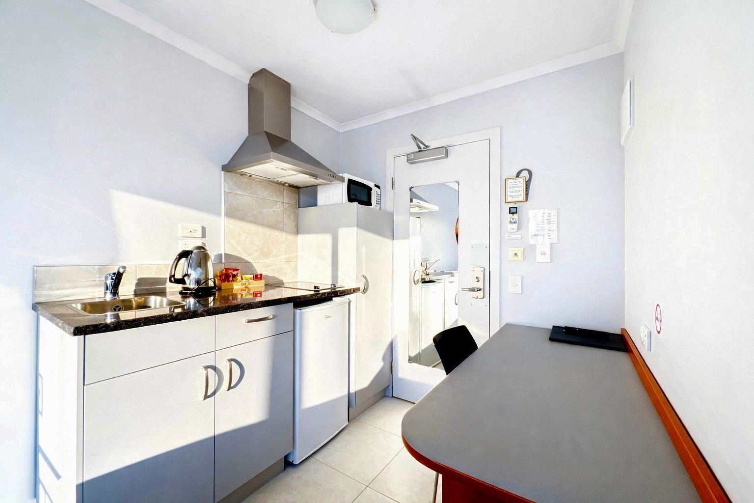 A compact kitchen with a sink, stove, and cabinets. There is a dining table with chairs and a door leading to another room.