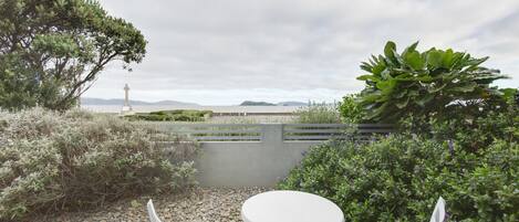 An outdoor seating area with a table and chairs, surrounded by greenery and a view of the sea.