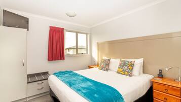 A hotel room with a bed, bedside table, lamp, and a window with curtains.