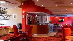 Un hall de hotel con zona de bar, asientos rojos y una planta grande.