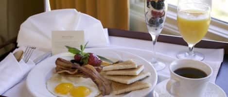 A breakfast tray with eggs, bacon, toast, a fruit parfait, a glass of orange juice, and a cup of coffee.