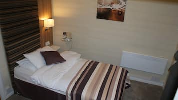 Una habitación de hotel con una cama, una mesita de noche, una lámpara, un cuadro en la pared y un radiador.