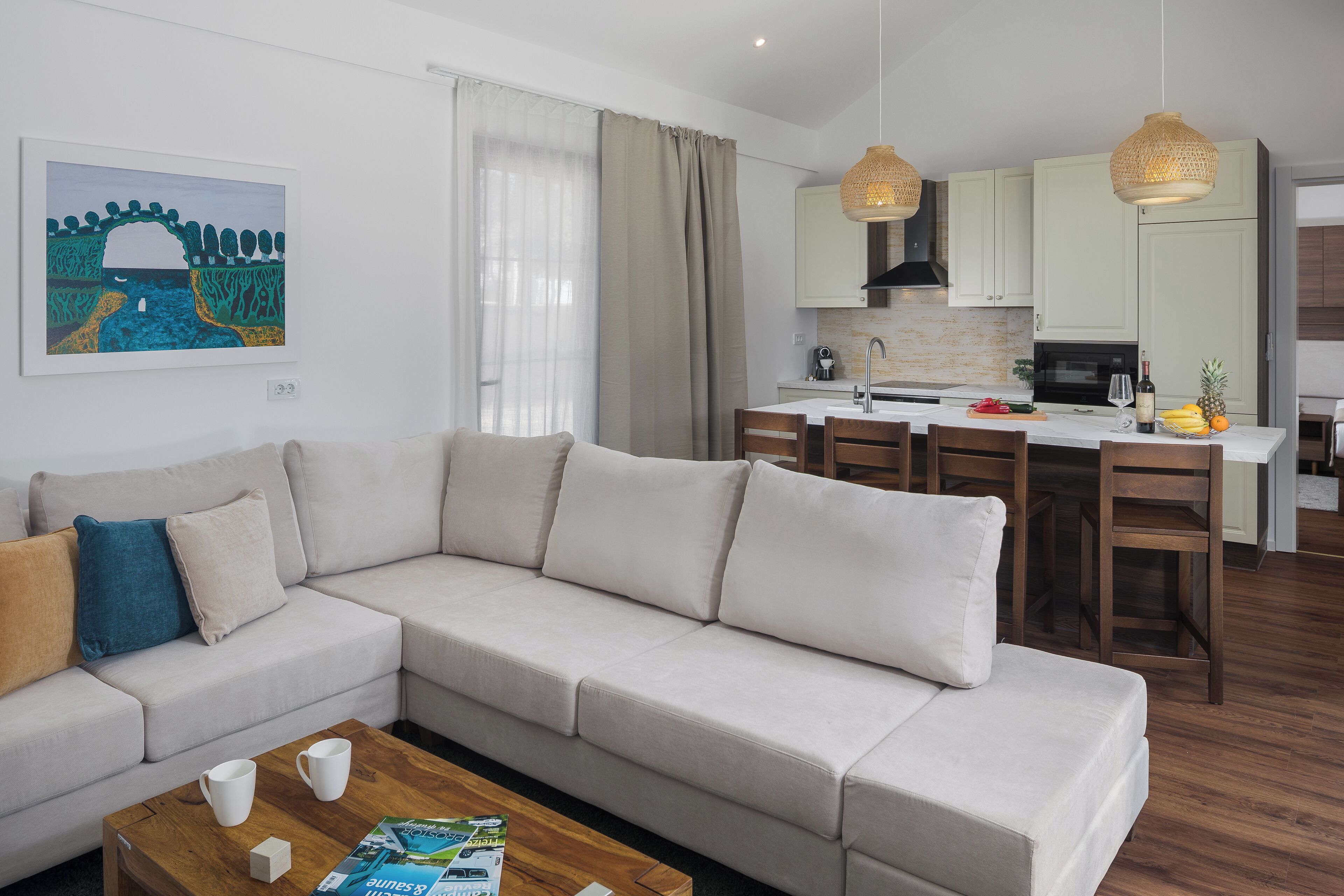 A modern living room with a sofa, coffee table, and artwork. A kitchen with a dining area is visible in the background.