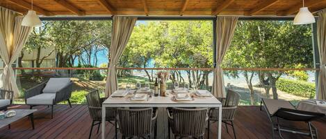A wooden deck with a table set for dining, surrounded by wicker chairs, overlooking a scenic view of trees and water.