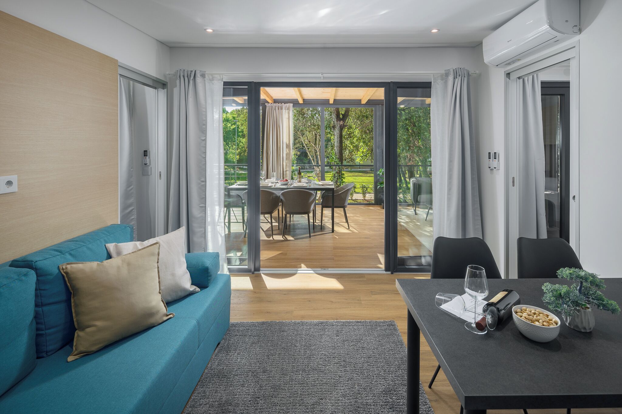 A modern living room with a blue sofa, a dining table with a bowl of nuts, and a view of an outdoor patio with a table and chairs.