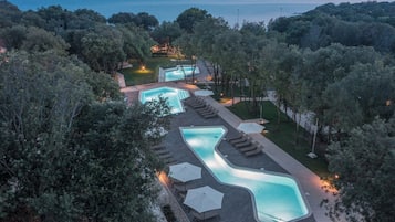 Vue aérienne d’un complexe hôtelier doté de plusieurs piscines, d’espaces de détente et bordé d’une forêt.