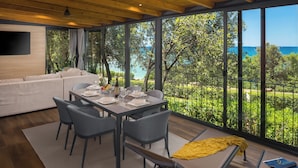 Uma zona de refeições moderna com uma mesa posta para quatro, um sofá e uma grande janela com vista para o mar.