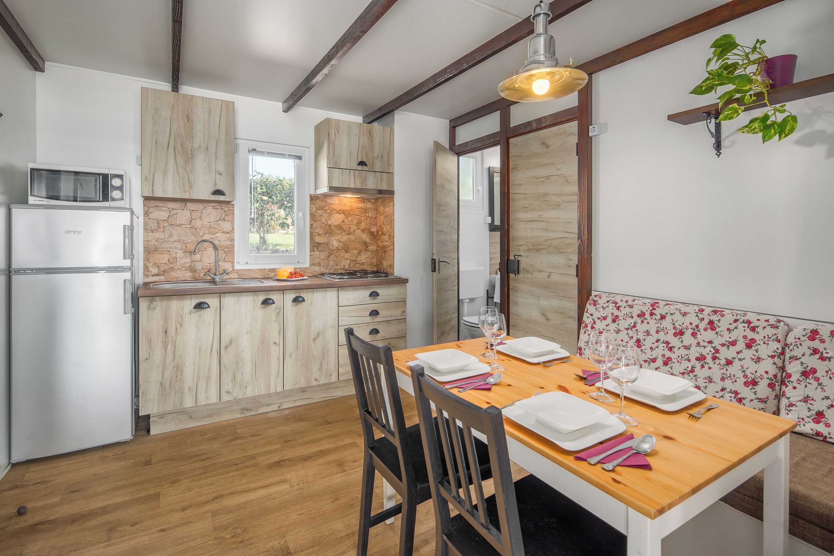 A kitchen with wooden cabinets, a stone backsplash, and a dining area with a wooden table set for four.