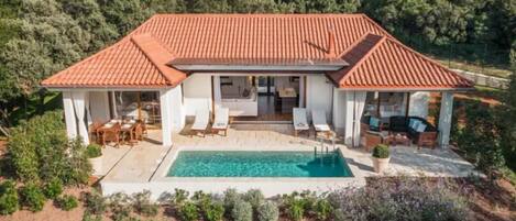 A two-story house with a swimming pool, outdoor seating, and a garden.