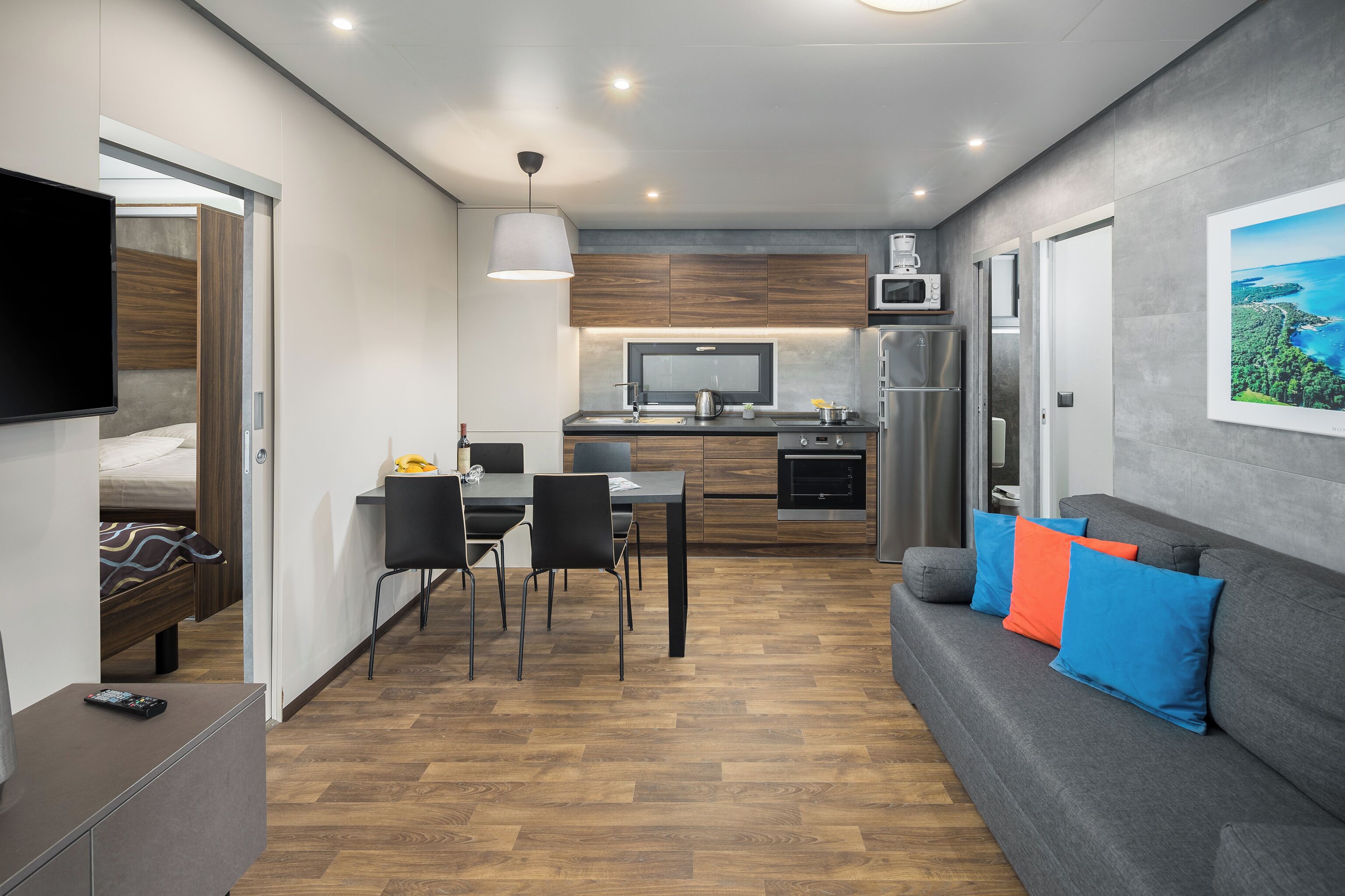 A compact living space with a kitchenette, a dining area, and a sofa with cushions.