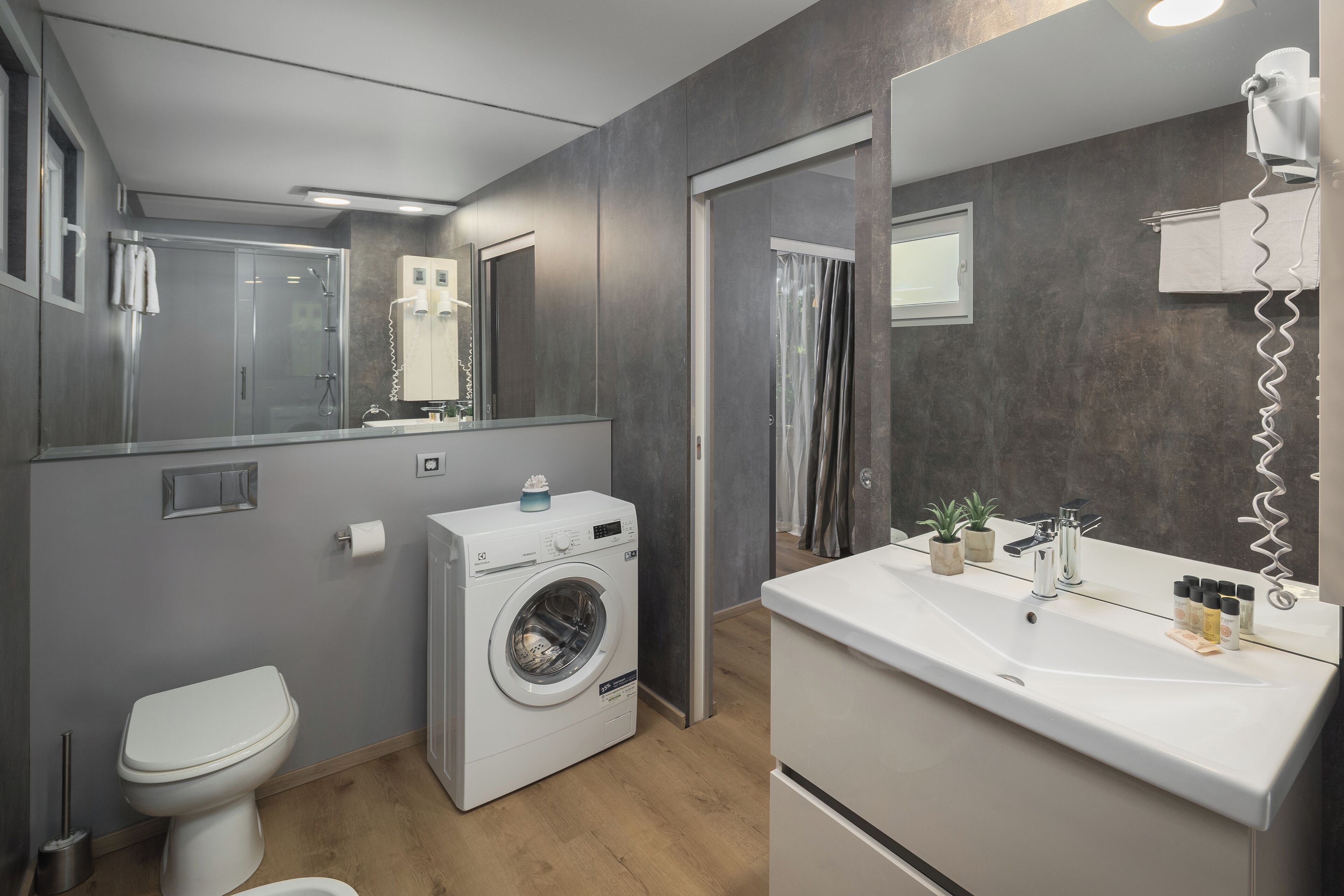 Un baño moderno con lavadora integrada, inodoro, lavamanos con espejo y zona de ducha.