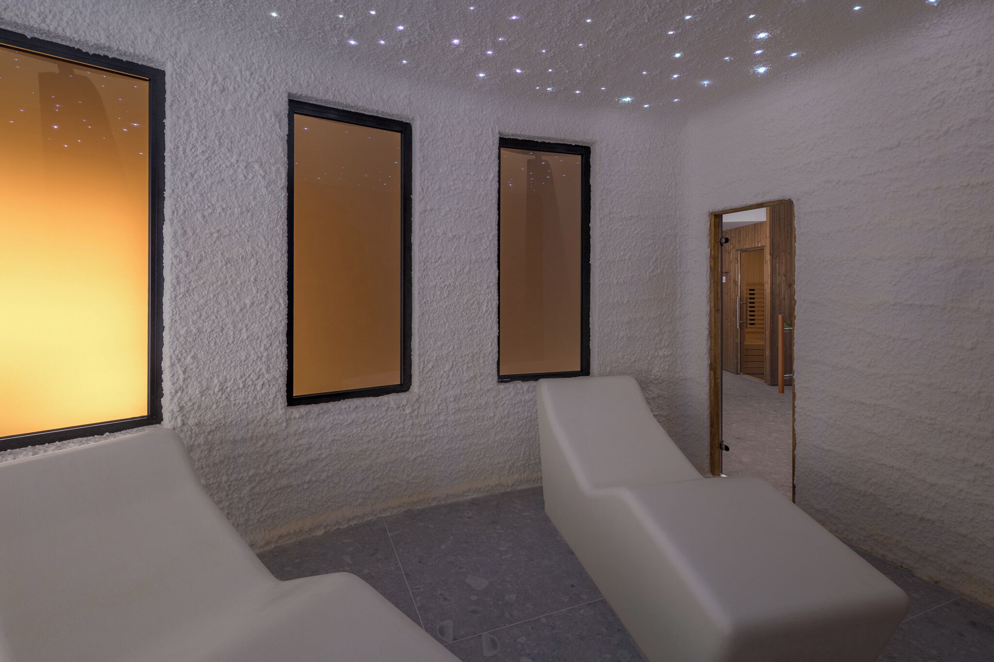 A spa room with a white textured wall, two large mirrors, and a wooden door.