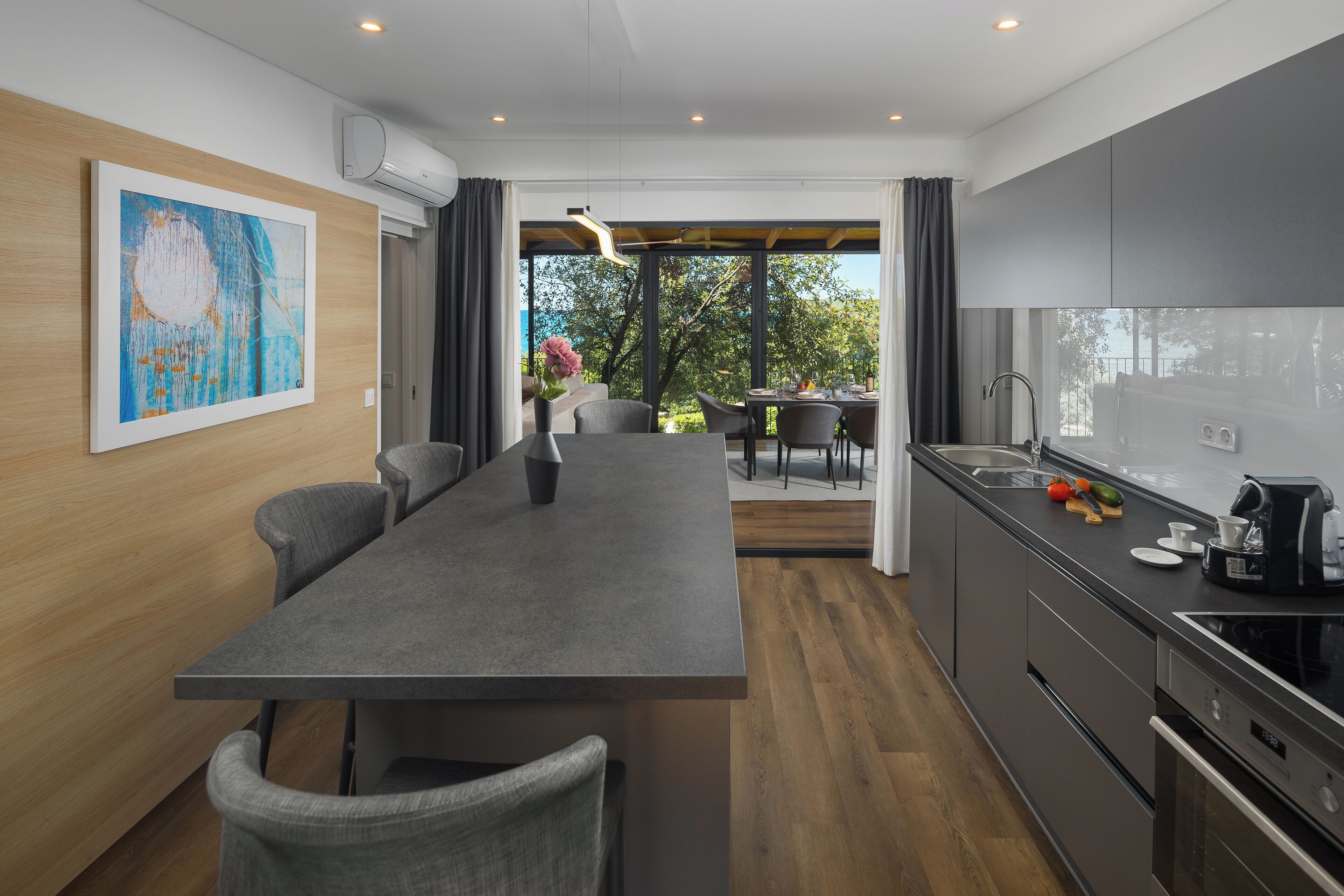 A modern kitchen with a central island, dark cabinetry, and a view to an outdoor dining area.