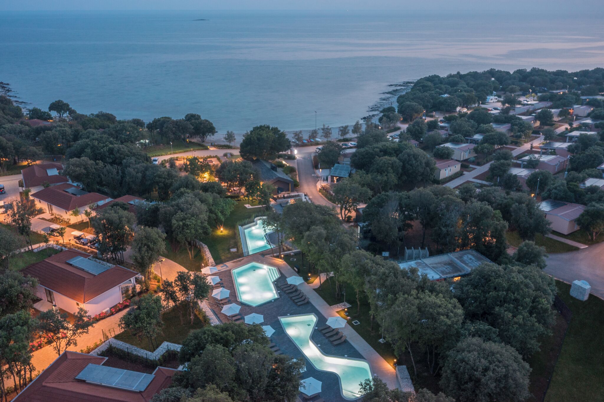 Eine Vogelperspektive zeigt einen Küstenort mit mehreren Swimmingpools, einer Marina und einer dichten Bebauung.