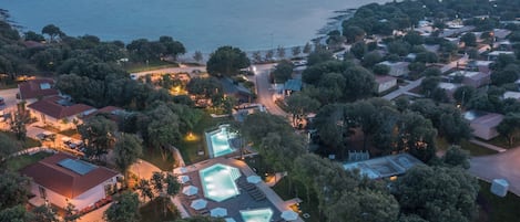Eine Vogelperspektive zeigt einen Küstenort mit mehreren Swimmingpools, einer Marina und einer dichten Bebauung.