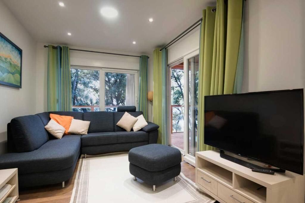A modern living room with a sectional sofa, ottoman, flat-screen TV, and a sliding glass door to the outdoors.