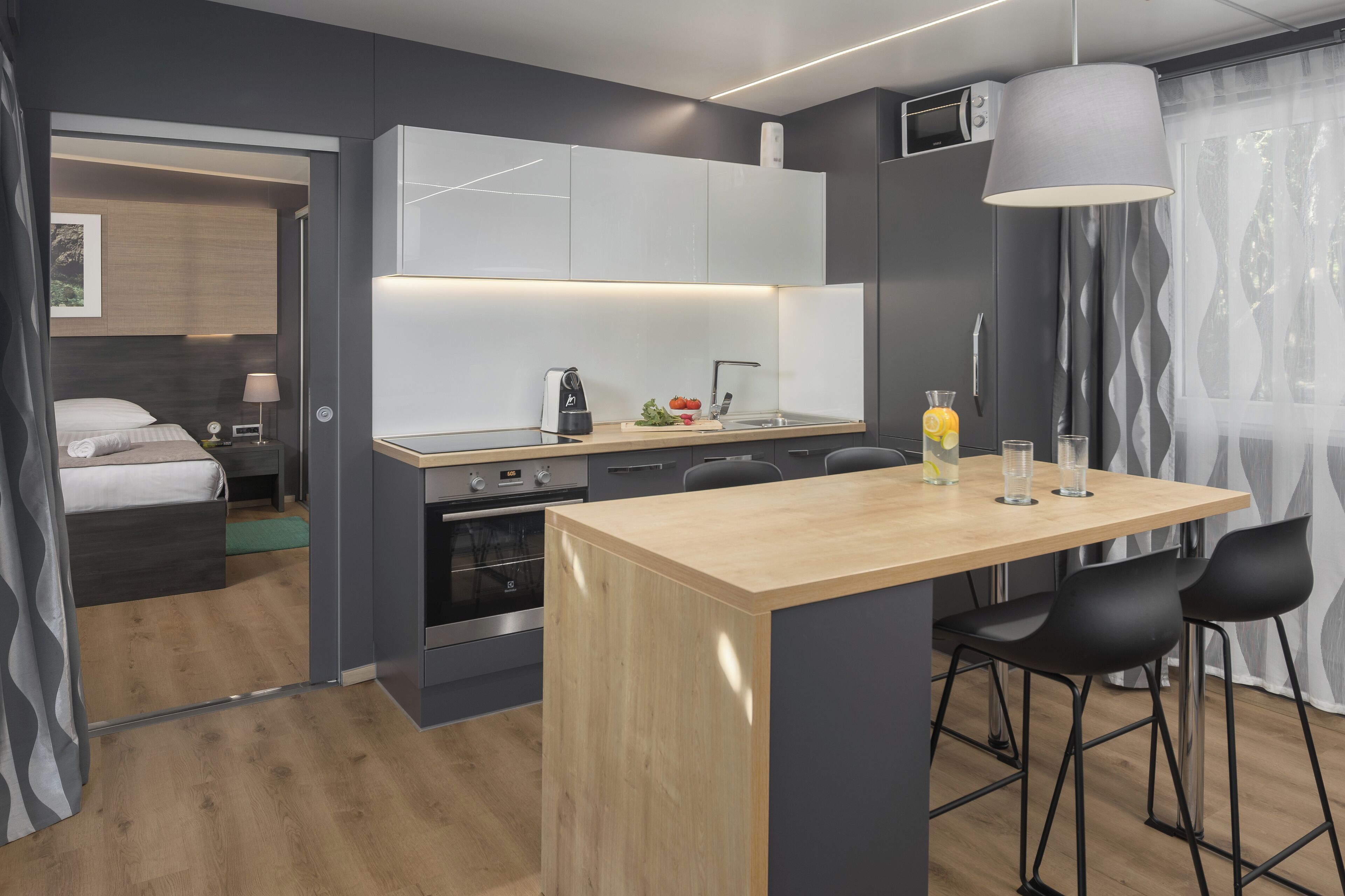 A modern kitchen with a central island, black bar stools, and a large pendant light.