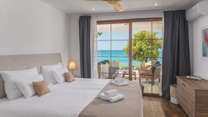 Quarto com cama grande, ventilador de teto e vista para o oceano através de uma porta de correr.