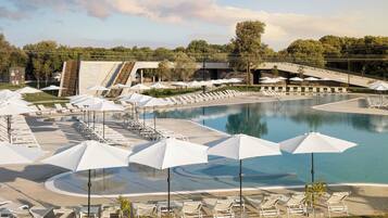 A pool area with lounge chairs and umbrellas, a waterfall feature, and a view of trees.