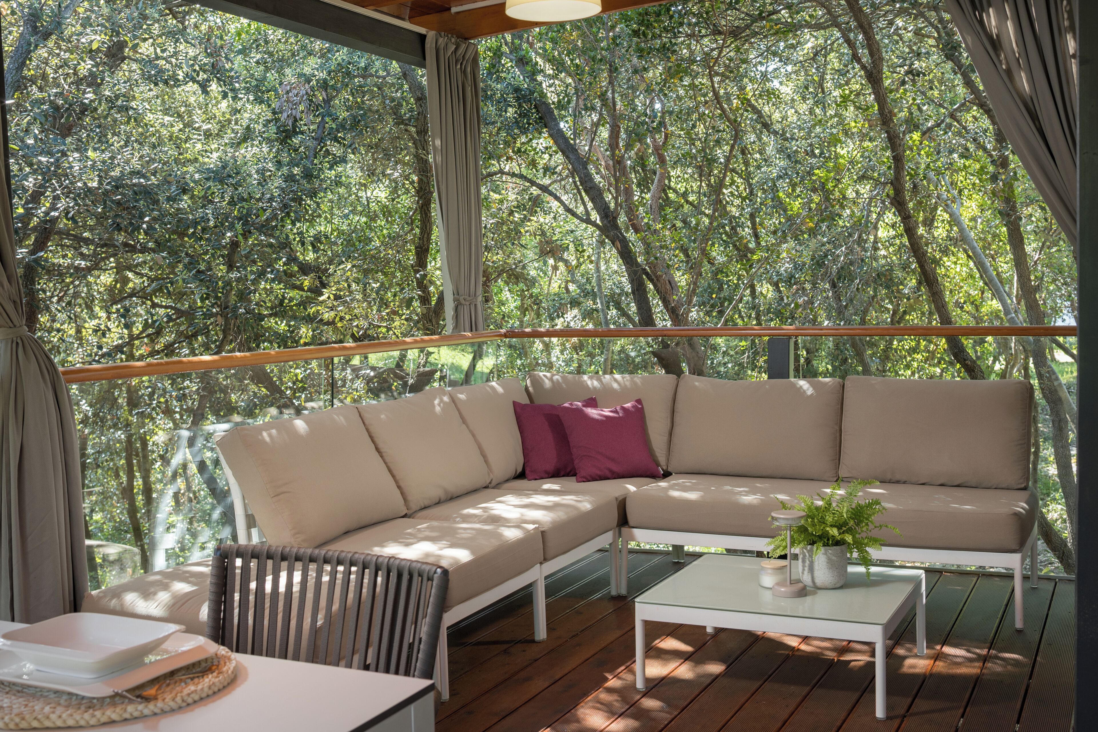 A covered outdoor seating area with a beige sofa, a white table, and a potted plant.