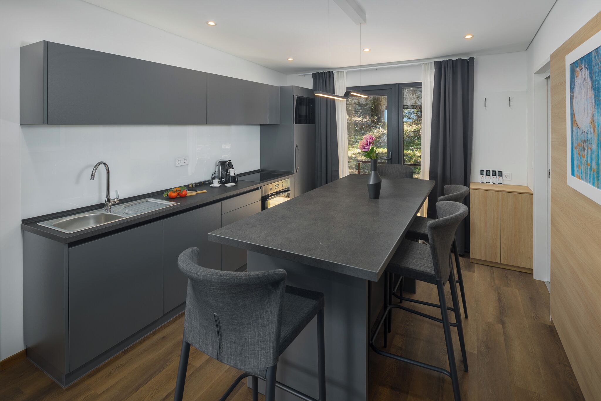 A modern kitchen with a central island, bar stools, a built-in sink, and a view of the outdoors.