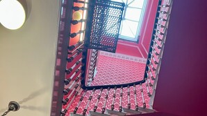 A room with a red carpet, a white wall with a decorative molding, and a window with a metal grid. - Eliza House (Edinburgh)