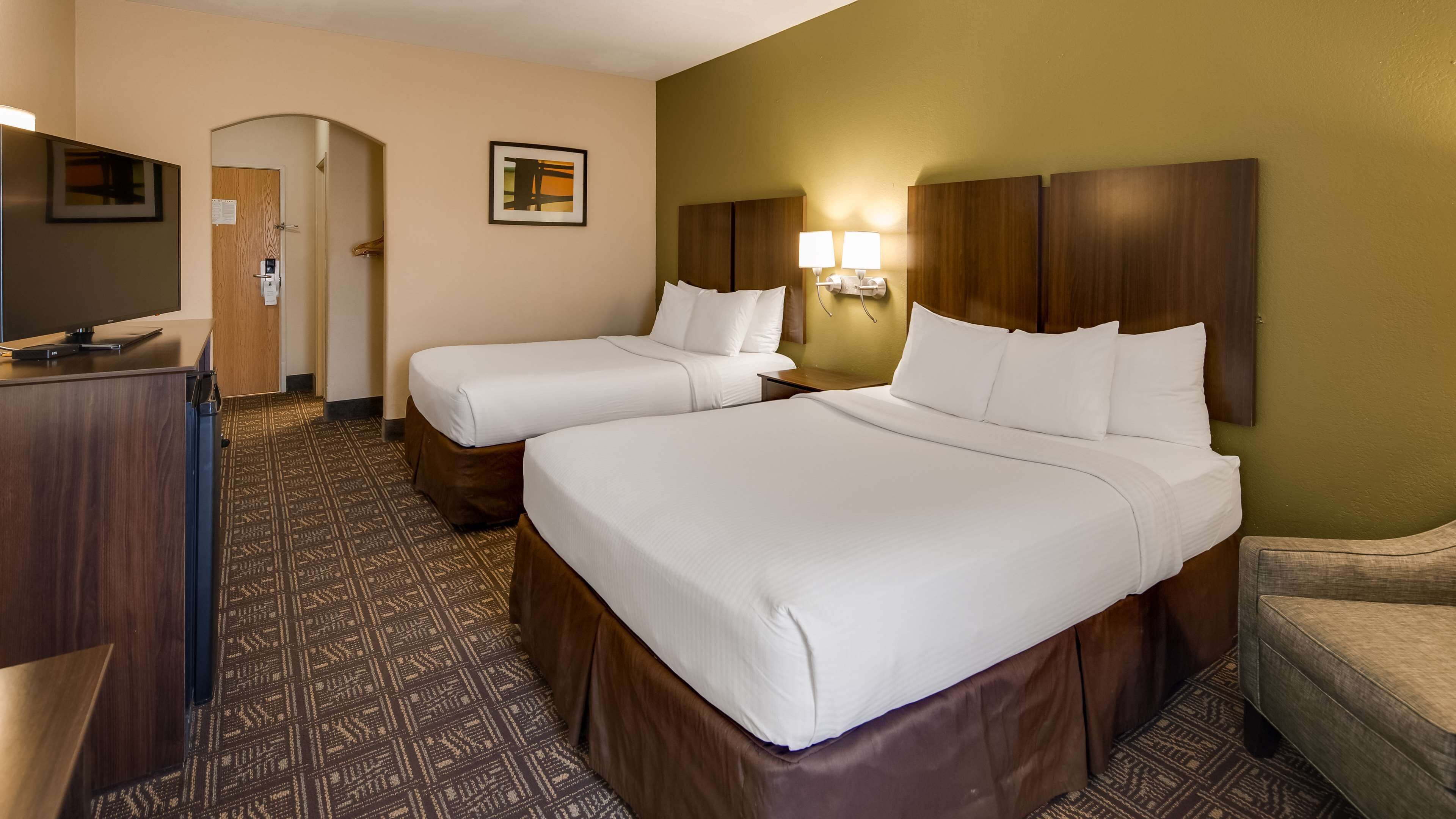 A hotel room with two beds, a desk, a TV, and a patterned carpet.