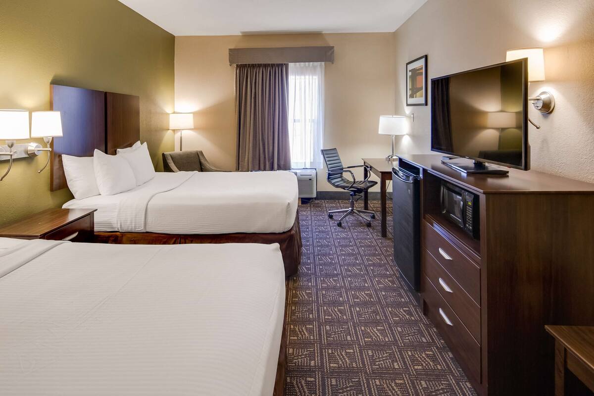 A hotel room with two beds, a desk with a television, a chair, and a desk lamp.