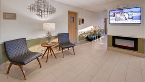 Een receptiegedeelte met twee leren fauteuils, een salontafel, een tv aan de muur en een open haard.