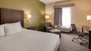 A hotel room with a large bed, two armchairs, a desk, and a window with curtains.