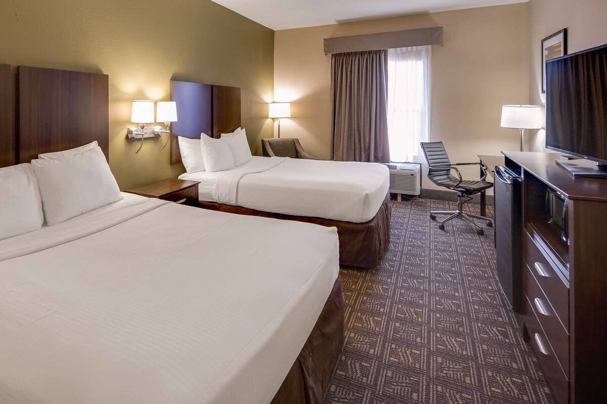 A hotel room with two beds, a desk with a chair, a TV, and a window with curtains.