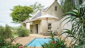 A house with a swimming pool, surrounded by lush greenery and a patio area with outdoor furniture. - RiverBend Lodge (Addo)