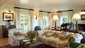 A living room with floral upholstery, a vintage trunk, and a decorative elephant statue. - RiverBend Lodge (Addo)