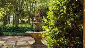A multi-tiered stone fountain in a garden with trees and greenery in the background. - RiverBend Lodge (Addo)