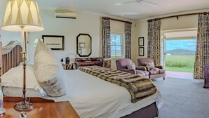 A bedroom with a large bed, a desk, a chair, a television, and a view of the outdoors. - RiverBend Lodge (Addo)
