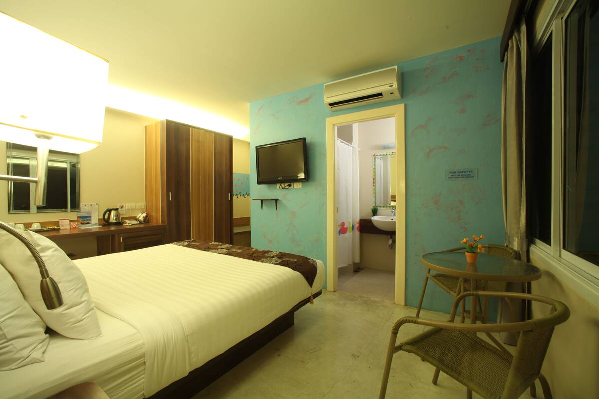 A hotel room with a bed, a desk, a chair, a television, and an air conditioning unit.