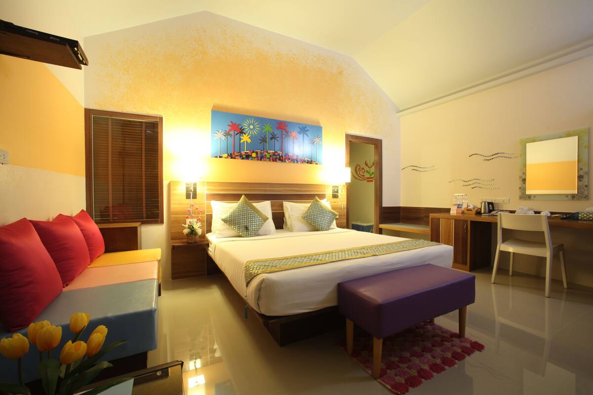 A hotel room with a bed, a desk, a chair, a couch, and a painting on the wall.