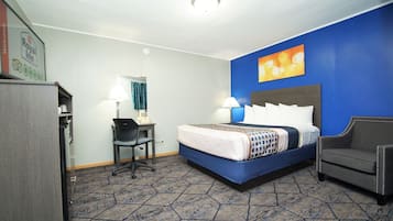 A hotel room with a bed, desk, chair, and a wall with a painting.
