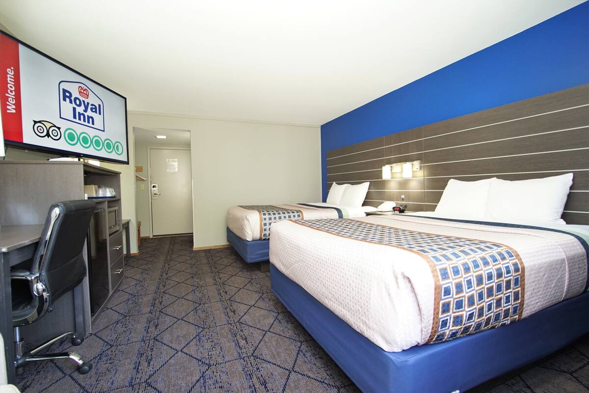 A hotel room with a bed, a desk, and a chair. There is a sign above the desk that says "Royal Inn Welcome".