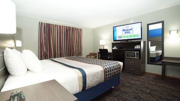 Una habitación de hotel con cama, escritorio, televisor mostrando el logotipo de Royal Inn, microondas, silla y cortina a rayas.