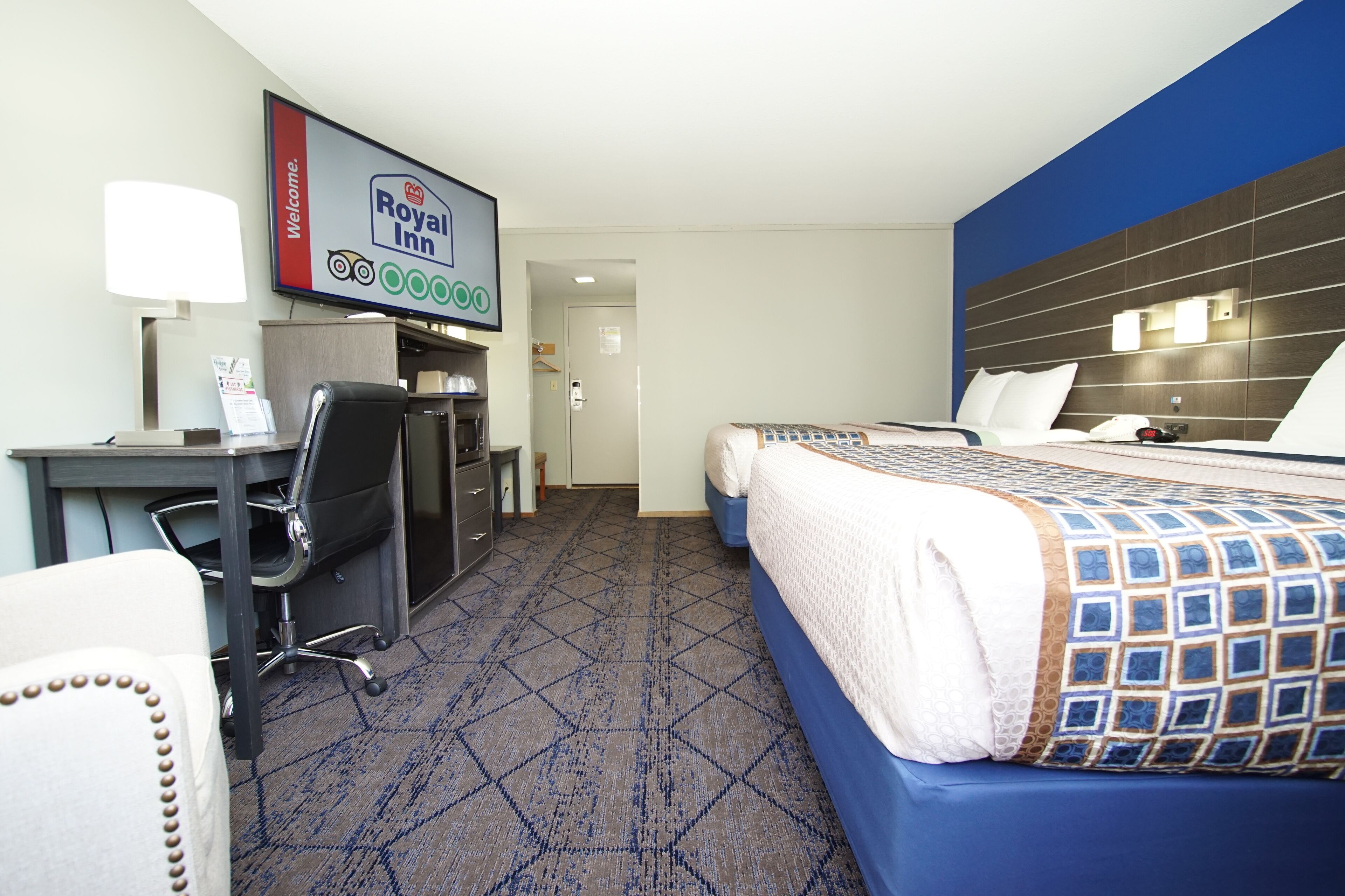 A hotel room with a bed, desk, chair, and a television displaying the Royal Inn logo.