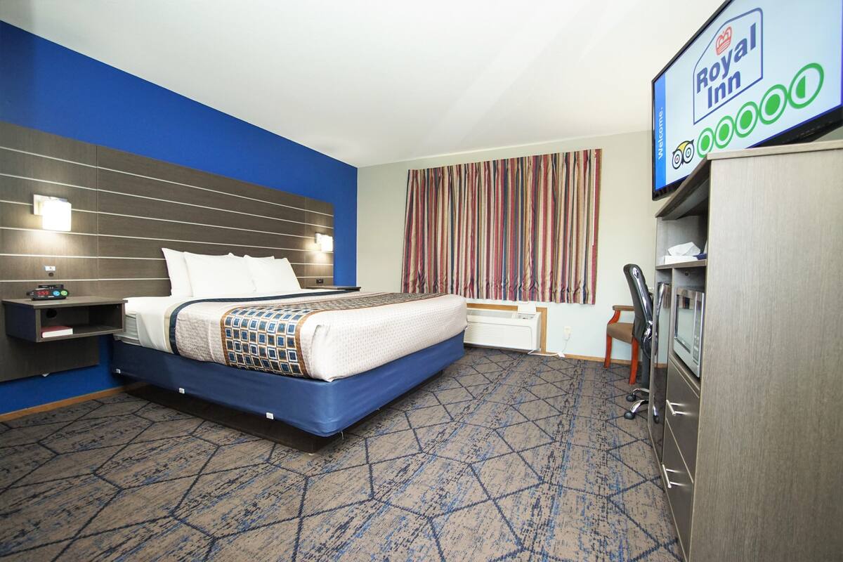 A hotel room with a bed, a desk, a TV, and a window with curtains.