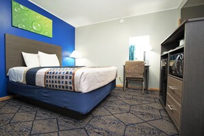 A hotel room with a bed, a desk, a chair, a wardrobe, and a wall with a green abstract painting.