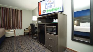 Une chambre d’hôtel équipée d’un lit, d’un bureau avec un ordinateur, d’un four à micro-ondes et d’un téléviseur affichant le logo de l’hôtel Royal Inn.