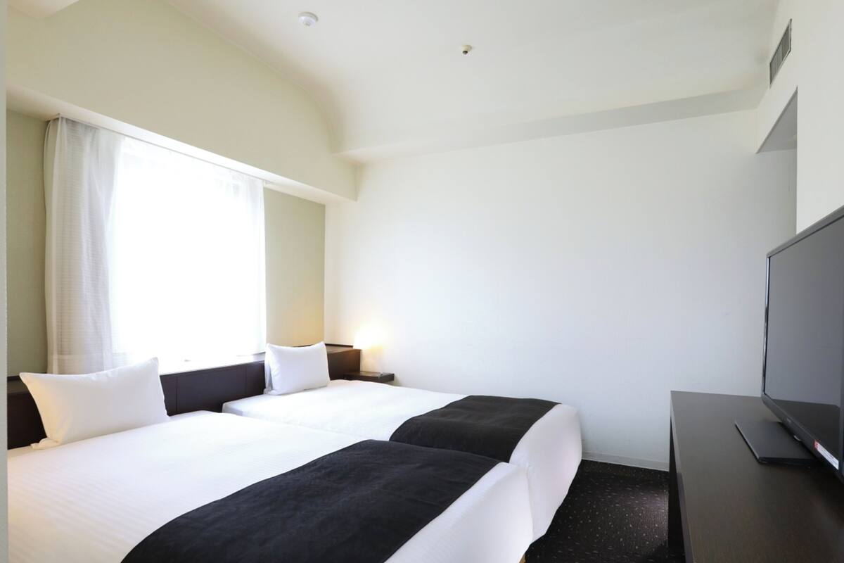 A hotel room with two beds, a TV, and a window with curtains.