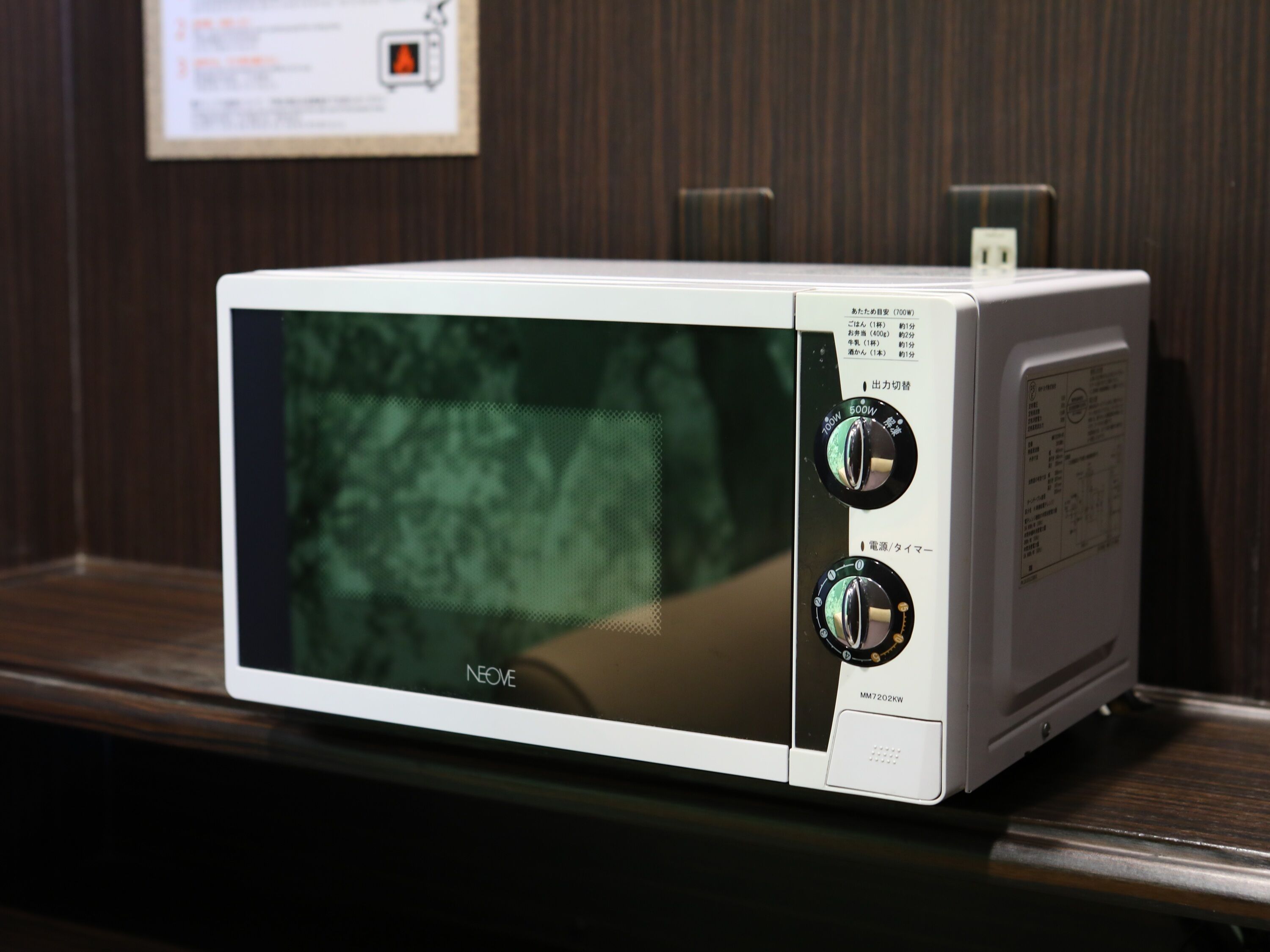 A white microwave oven with two dials and a digital display, placed on a wooden surface.
