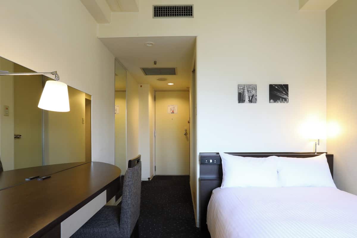 A hotel room with a bed, a desk, a chair, a lamp, and a water dispenser.