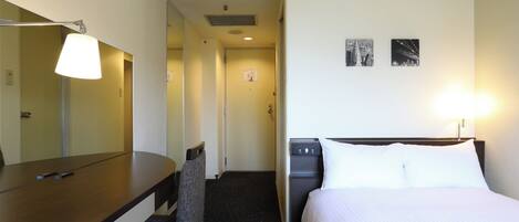 Quarto de hotel com uma cama, uma escrivaninha, uma cadeira, um abajur e um dispensador de água.